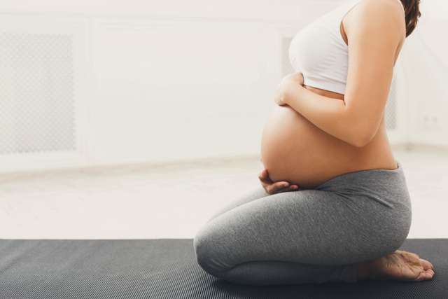 Pregnant woman sitting on a yoga mat Unrecognizable pregnant woman practicing yoga in hero pose, caressing her belly. Young happy expectation relax, think about her baby and her future