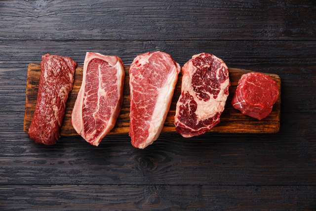 Red meat is presented on a wooden board Variety of Raw Black Angus Prime Meat Steaks Machete, Blade on Bone, Striploin, Rib eye, Tenderloin Filet Mignon on Wooden Board Copies Room