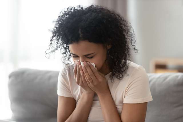 Woman with allergic symptoms. Ill angry African woman blowing runny nose, got flu that settled in tissues, sick allergic black woman with allergic symptoms coughing a napkin at home, hay fever concept