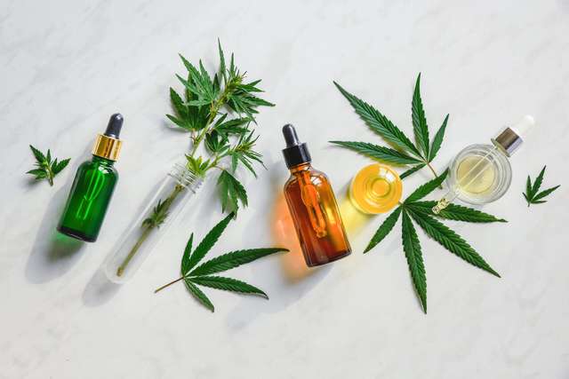Different glass bottles of CBD oil. Various glass bottles with CBD oil, THC tincture and hemp leaves on marble background. Flat position, minimalism. Cosmetics CBD oil.