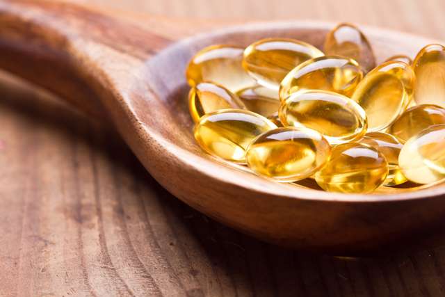 Omega-3 gel capsules in a wooden spoon. Cod liver oil omega 3 gel capsules single on wooden background