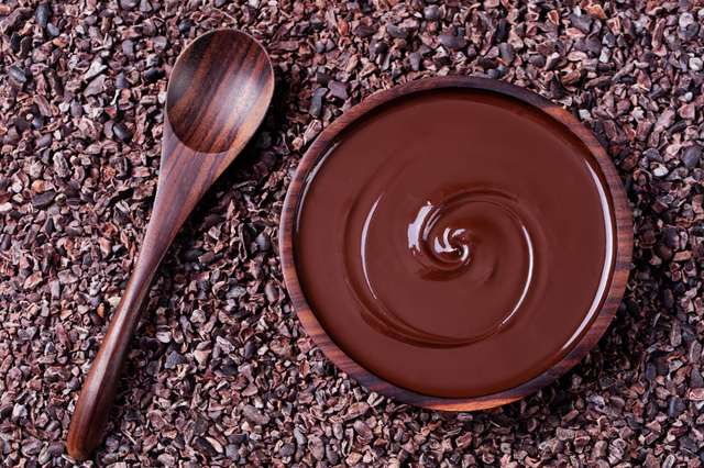 Spoon and a bowl of melted chocolate on cocoa beans. Spoon and a bowl of melted chocolate on cocoa beans.