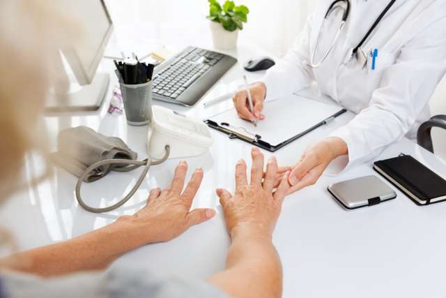Medical examination with older woman showing her hands to the doctor. Close up of medical examination.middle aged woman with arthritis showing hands to female doctor.