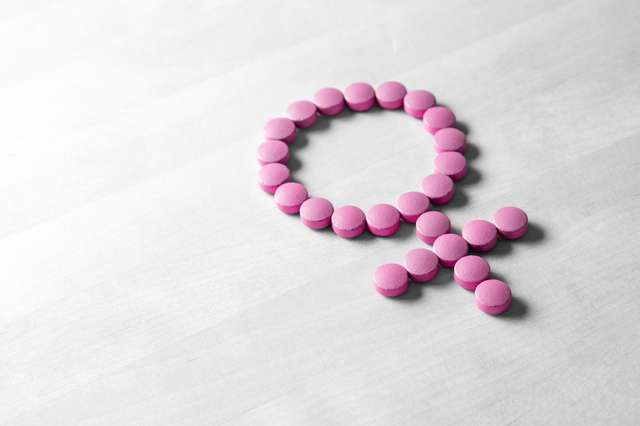 Sex symbol made of pink red pills or tablets on wooden table. Sex symbol made of pink red pills or tablets on wooden table.