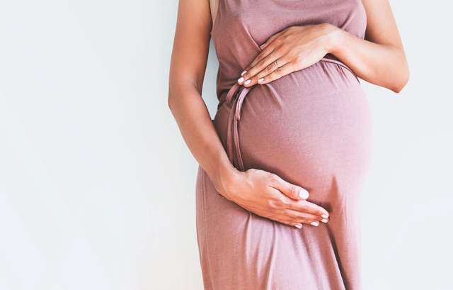 Pregnant woman in clothes holds hands on belly on white background. pregnancy, maternity, preparation and expectation concept. Close up, copy room, inside. Beautiful delicate mood image of pregnancy. A pregnant woman holds her belly. The background is white.