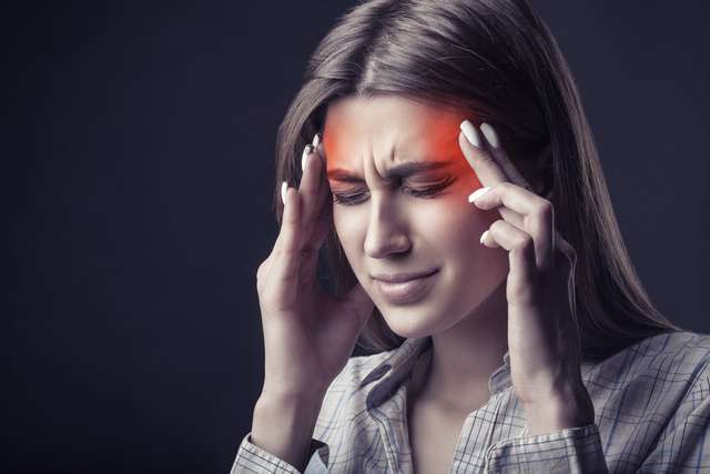 Young woman suffers from headaches Young woman suffering from headache on dark background. Studio shot