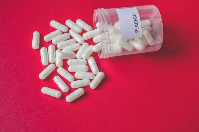 White tablets in a clear placebo-labeled container. White placebo pills or capsules spilling out of a bottle on red background, placebo effect, randomization or treatment concept, vintage view