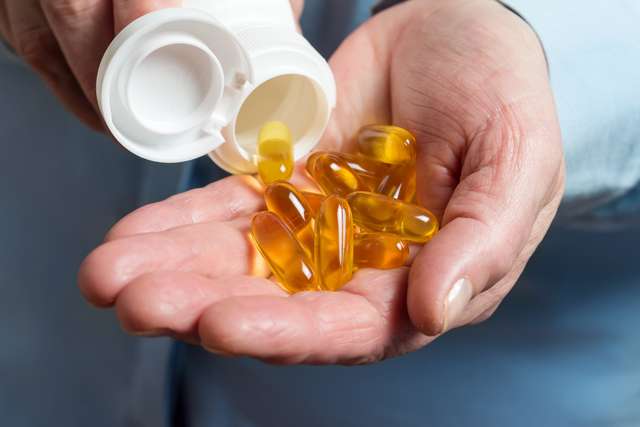 A person holds several omega-3 capsules in his left hand. The female hand holds yellow medicine capsules of Omega 3, Greeks from a white bottle in palm the fish oil, healthy instruction leaflet.