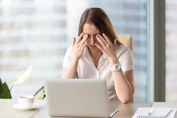 Joven mujer de negocios haciendo ejercicios en el trabajo para cansar los ojos de la computadora, el masaje de los párpados cerrados para relajar los músculos, reducir la tensión, mejorar la visión, el yoga para la fatiga ocular, la relajación de los ojos Una empresaria en su puesto de trabajo en la oficina se masajea los párpados para relajarse.