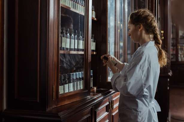Pexels Frau öffnet einen Apotheker-Schrank aus Holz und Glas und inspiziert ein Arzneimittel.