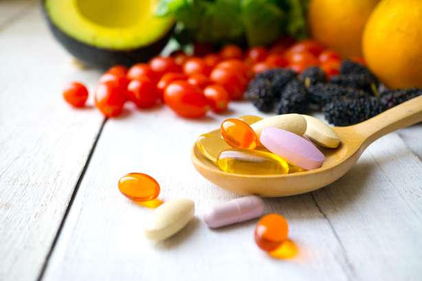 Comprimidos e cápsulas em uma colher de madeira com frutas frescas ao fundo. Comprimidos e cápsulas em colher de pau com fruta fresca. Multivitaminas e suplemento a partir do conceito de fruta.