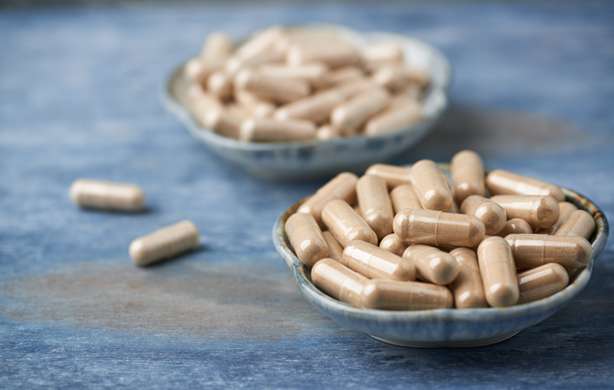 Una ciotola piena di capsule. Capsule di Ashwagandha (Withania somnifera) e Ginseng coreano. Concetto per una sana integrazione alimentare. Sfondo rustico in legno. Copiare lo spazio.