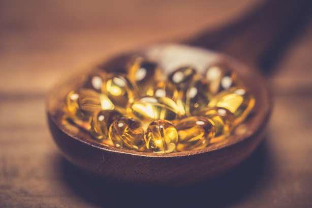 Omega-3 gelcapsules gemaakt van levertraan, geïsoleerd op een houten basis. Vitamine D capsules. Voedingssupplement Vitamine D capsules in een houten lepel op een houten tafel.