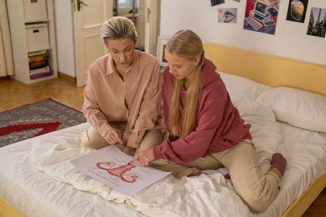 pexels/cottonbro/6471427 An older and younger woman sit and discuss an image of a human uterus.