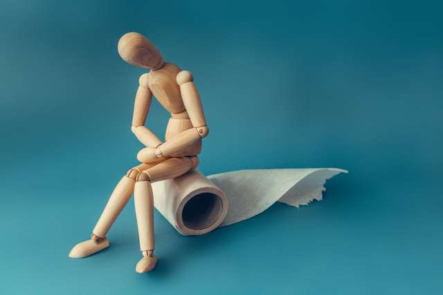 A wooden figure sits on a roll of toilet paper. A wooden figure sits on a roll of toilet paper. Concept of the problem with digestion.