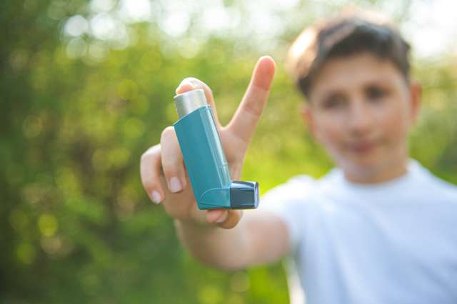 Asthma Welttag. Ein Mann hat einen Asthmamagenten in den Händen auf den Parkhintergründen. Der Junge im weißen T-Shirt mit Asthma-Inhalator. Ein Junge im weißen T-Shirt haltet einen Asthma Inhalator in die Kamera. Im Hintergrund ist sonnige Natur.