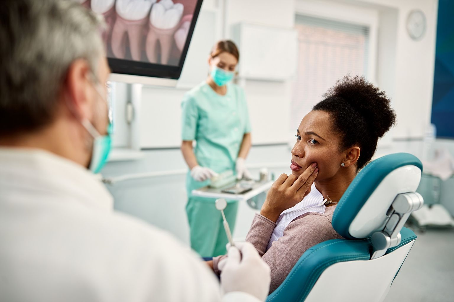 Une femme montre à un dentiste dans la salle de soins l'endroit de sa bouche où elle a mal aux dents.